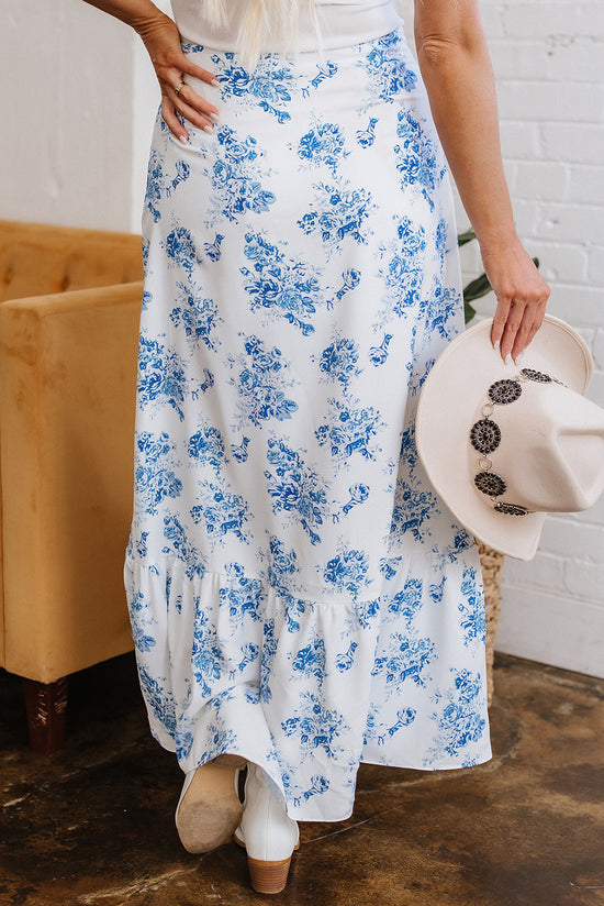 Woman in floral skirt holding a hat.