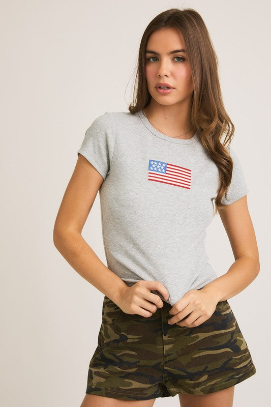 Woman in gray t-shirt with American flag graphic and camo shorts.