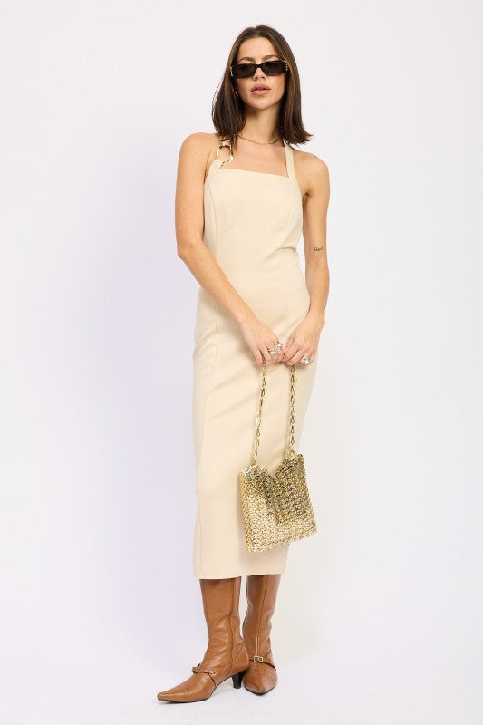 Woman wearing a beige dress holding a gold handbag on a white background