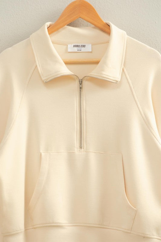 Beige sleeveless jacket with a quarter zip on a wooden hanger against a light background