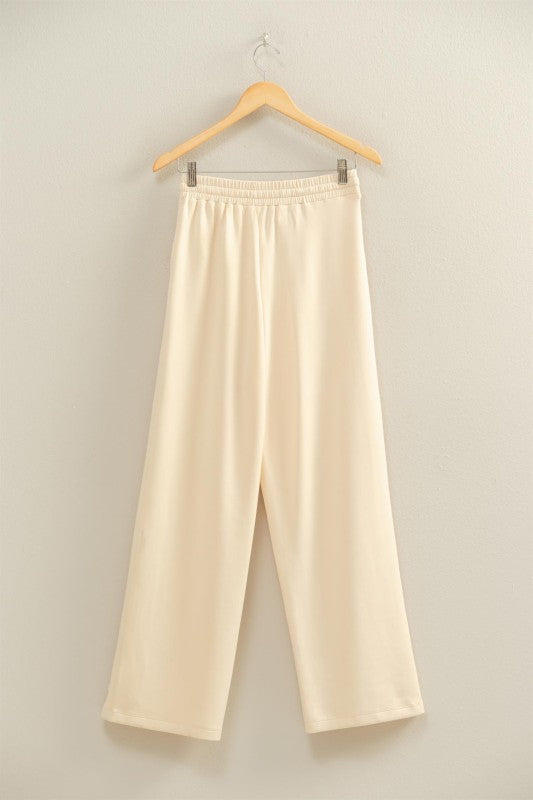 Beige pants hanging on a wooden hanger against a plain background