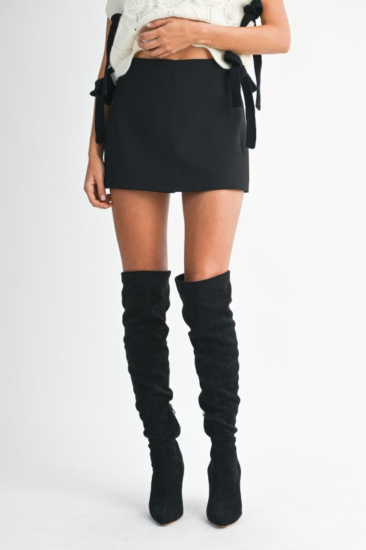 Person wearing a black mini skirt and knee-high black boots on a white background