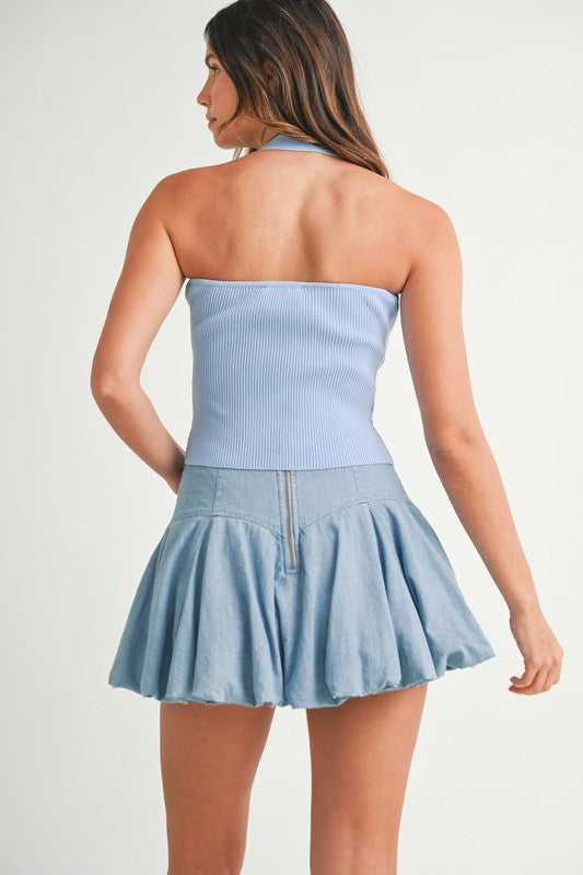 Woman in blue halter top and denim skirt.