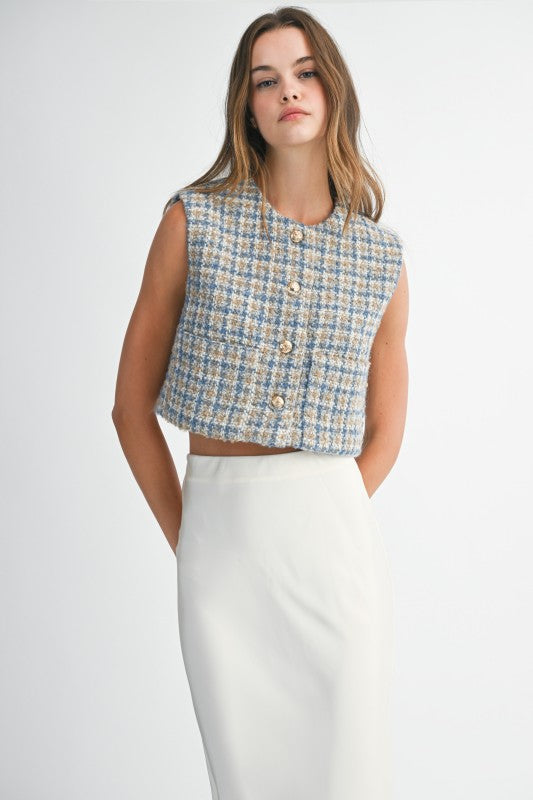 Woman wearing a sleeveless checkered top and white skirt on a plain background