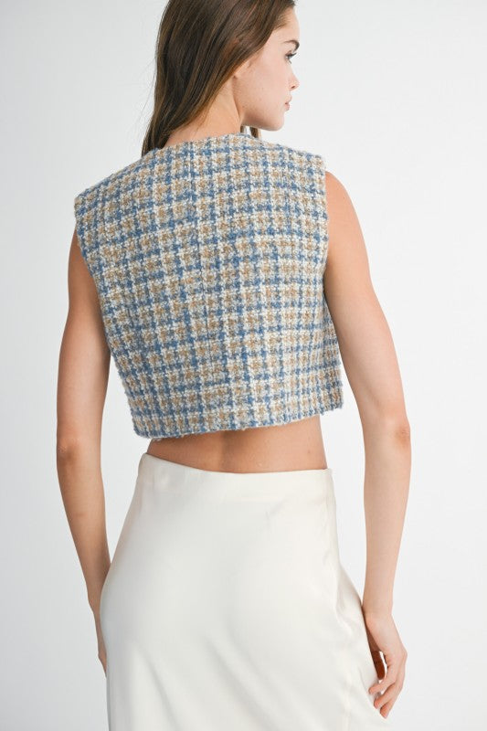 Woman wearing a patterned crop top and white pants on a plain background