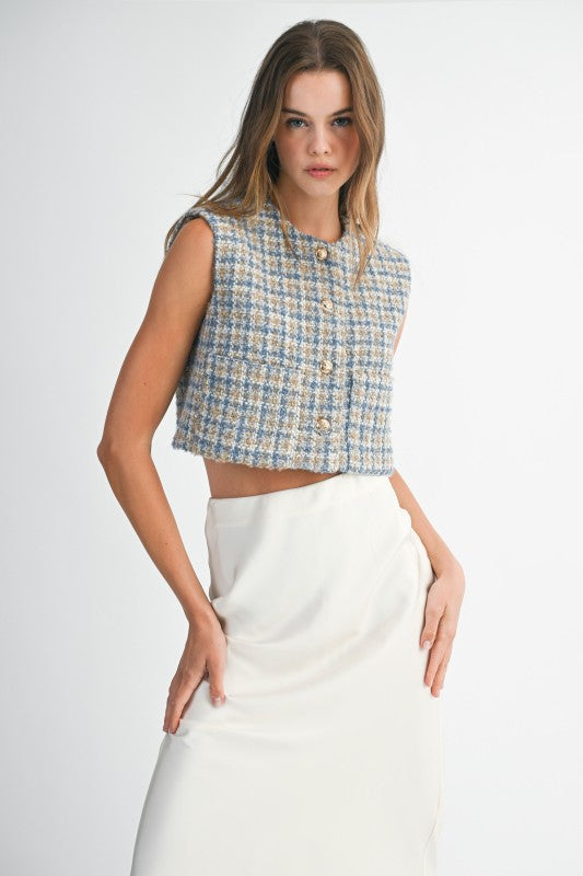 Woman wearing a sleeveless checkered top and white skirt on a plain background