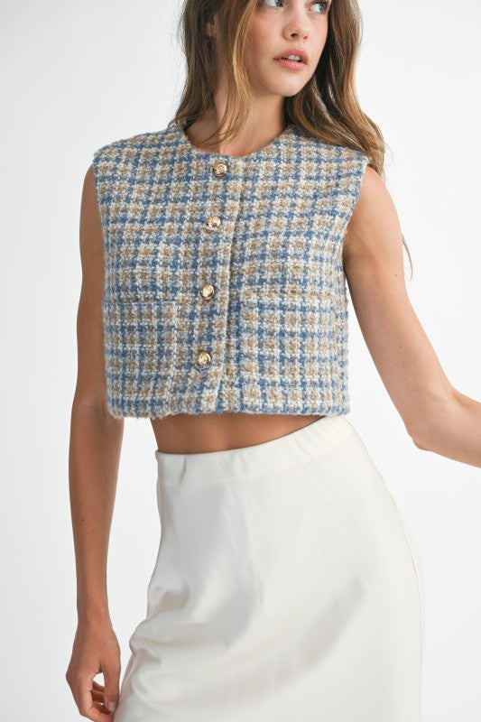 Woman wearing a blue and beige checkered vest over a white top on a white background