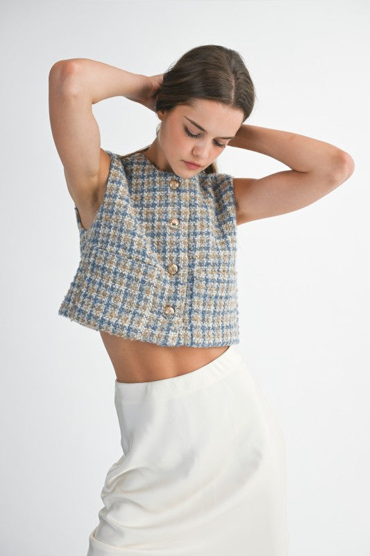 Woman wearing a patterned sleeveless top and white pants on a plain background