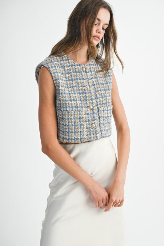 Woman wearing a sleeveless patterned top and white pants on a plain background