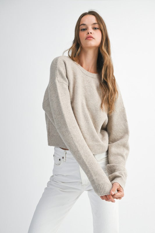 Woman wearing a beige sweater and white pants on a light gray background