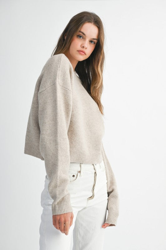 Woman wearing a beige sweater and white pants on a plain background