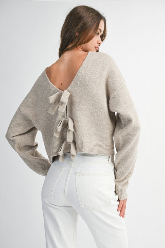Woman wearing a beige sweater with bow details on a white background