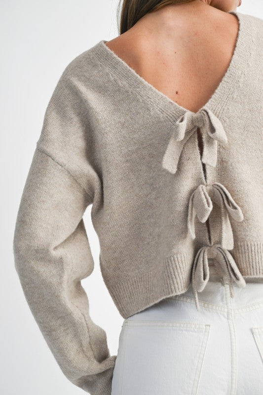 Beige sweater with tie details on a plain background