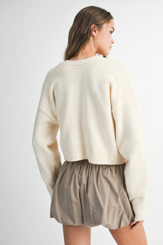 Woman wearing a cream sweater and beige shorts on a white background