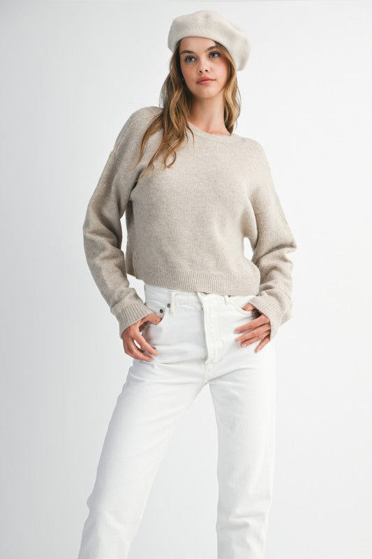 Woman wearing a beige sweater and white pants on a plain background
