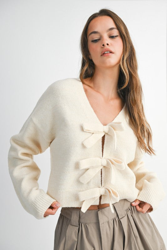 Woman wearing a cream-colored cardigan with ruffle details on a white background