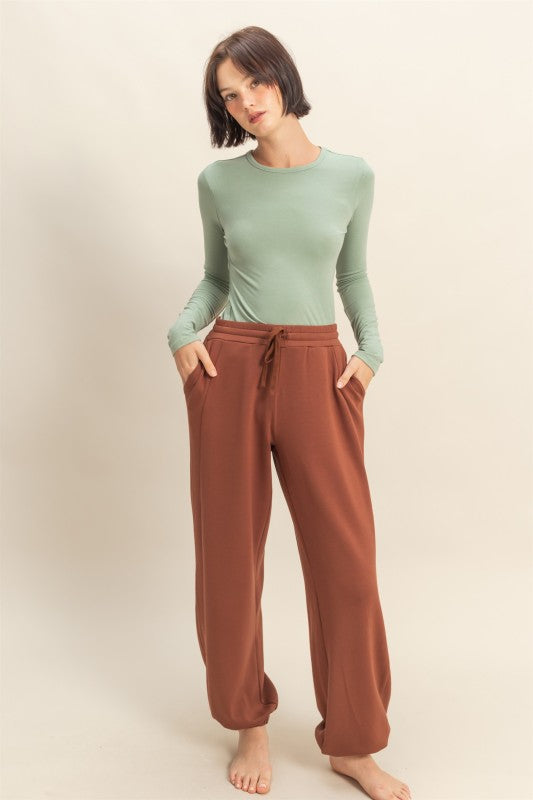 Woman wearing a green long-sleeve top and brown pants on a beige background