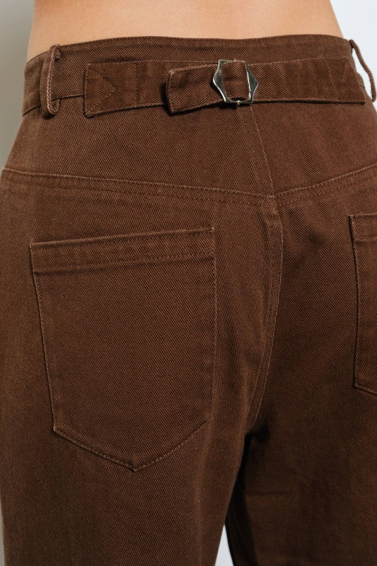 Close-up of brown pants with a belt buckle on a neutral background