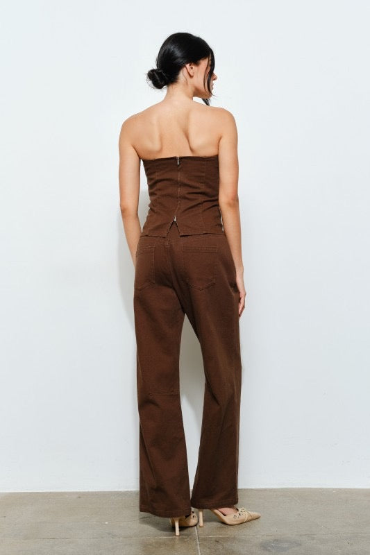 Woman wearing a brown strapless jumpsuit against a white wall.
