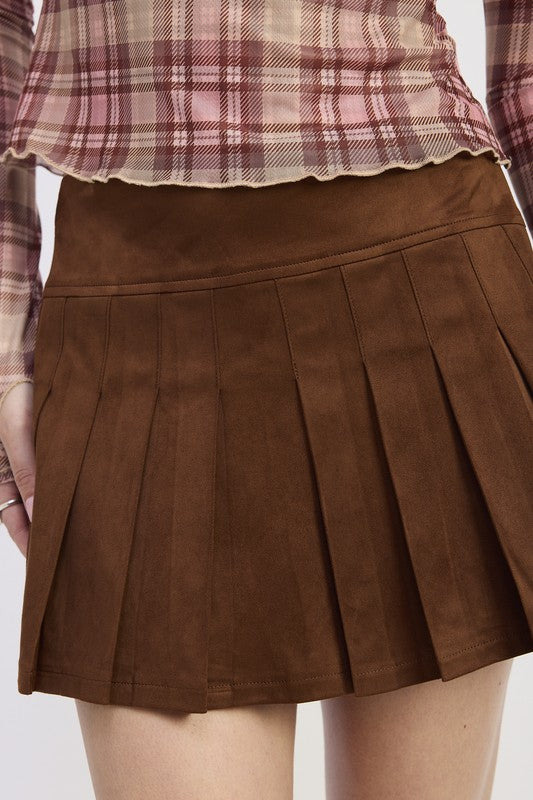 Brown pleated skirt worn with a plaid shirt on a white background