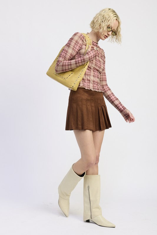 Person wearing a plaid shirt, brown skirt, and white boots with a yellow bag on a light gray background