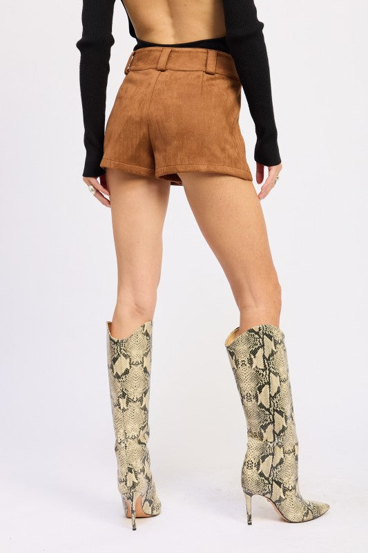 Person wearing tan suede shorts and snake print knee-high boots on a white background