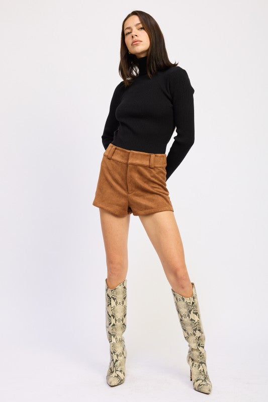 Person wearing a black turtleneck, brown shorts, and patterned knee-high boots on a white background