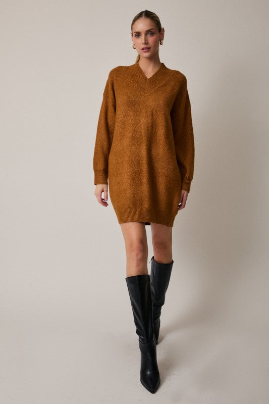 Woman wearing a brown sweater dress and black knee-high boots on a plain background