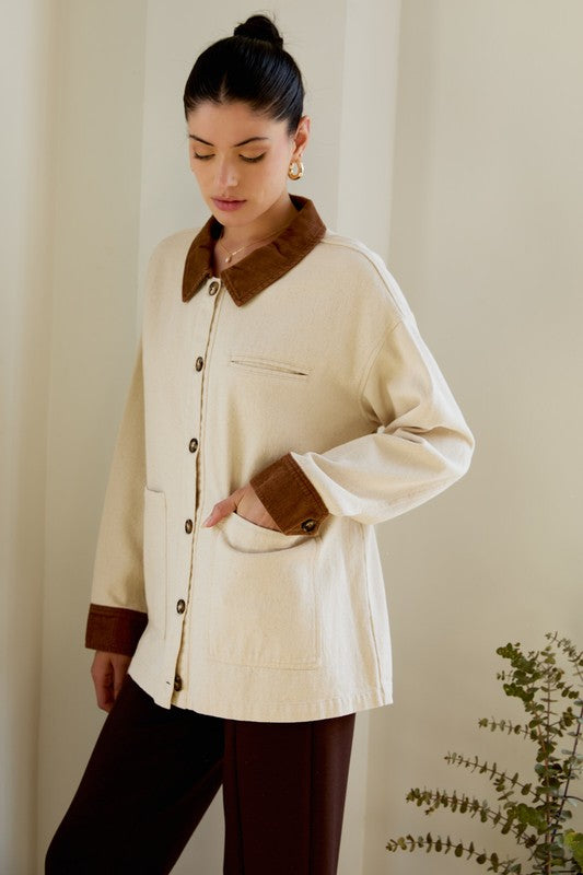 Woman wearing a cream jacket with brown collar and cuffs against a neutral background