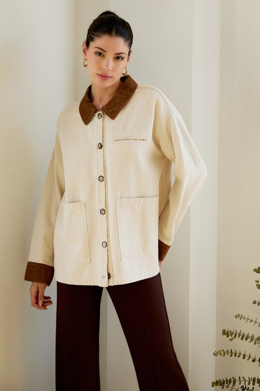 Woman wearing a cream jacket with brown collar and cuffs against a neutral background