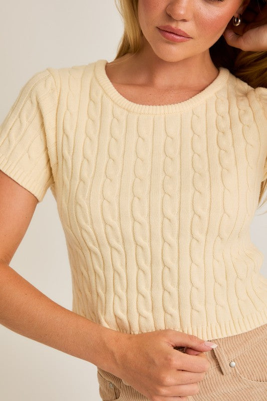 Woman wearing a beige cable knit sweater against a neutral background