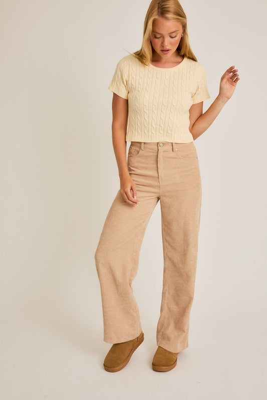 Woman wearing a beige top and pants on a plain background