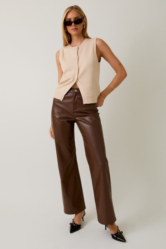 Woman wearing a beige sleeveless top and brown leather pants on a white background