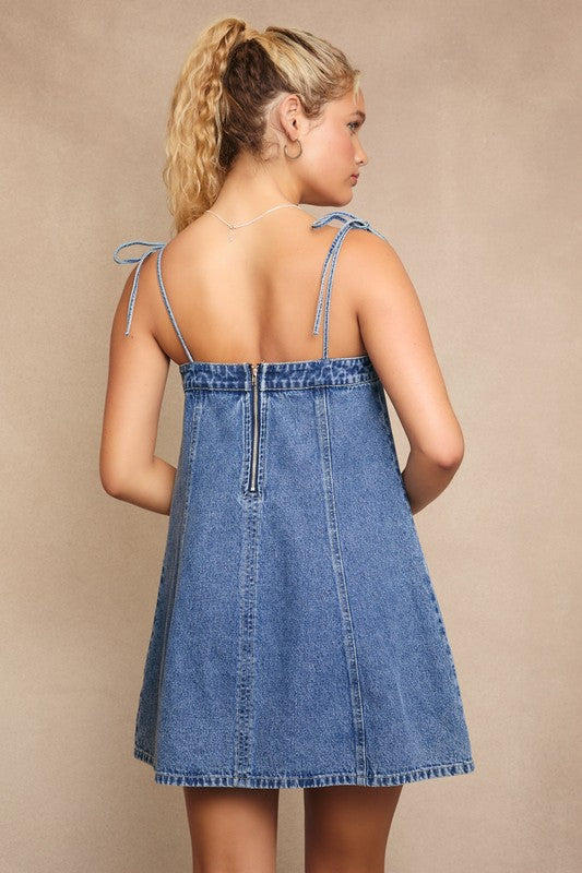 Woman wearing a denim dress with thin straps on a beige background