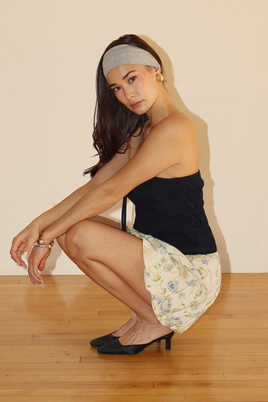 Woman squatting in a black top and floral skirt.