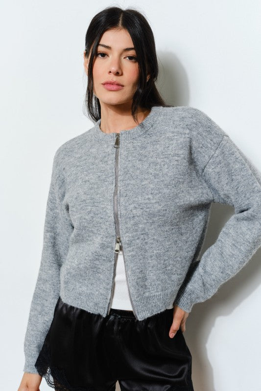 Woman wearing a gray zip-up sweater against a white background
