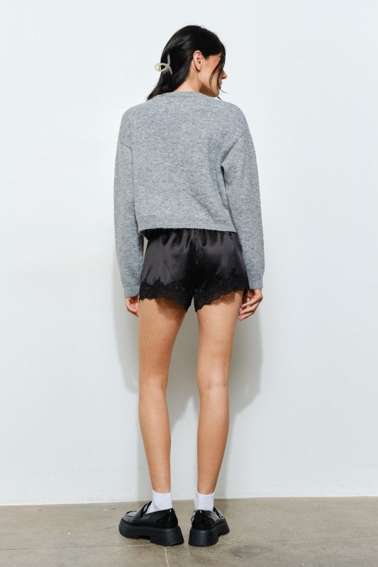 Person wearing a gray sweater and black shorts against a white wall