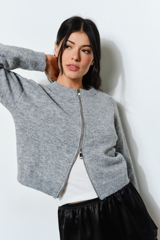 Woman wearing a gray cardigan over a white shirt with a black skirt against a white background