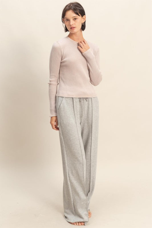 Woman wearing a light pink sweater and gray pants on a beige background