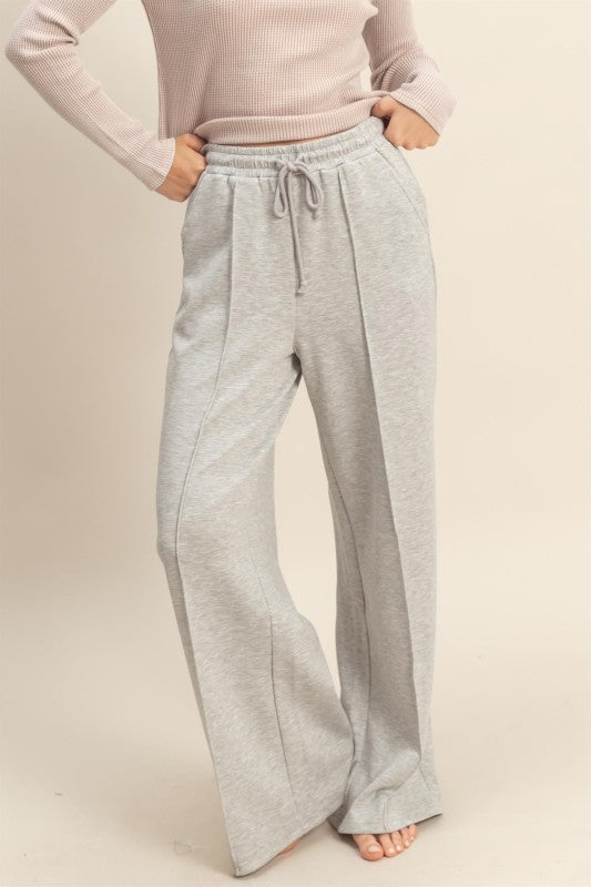 Person wearing light gray sweatpants and a pink top on a beige background