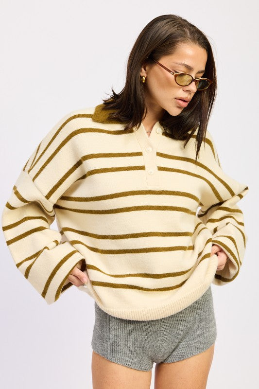 Woman wearing a cream and brown striped sweater with gray shorts on a white background