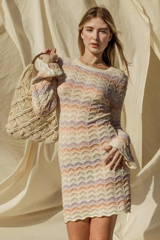 Woman wearing a colorful knit dress holding a woven bag against a neutral background