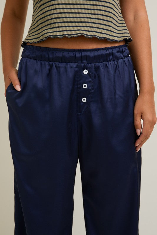 Navy blue pants with white buttons worn by a person on a neutral background