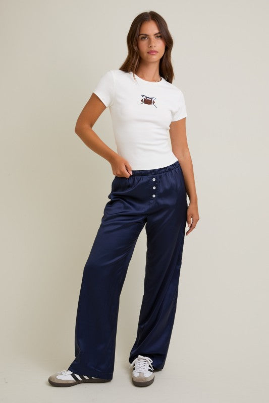 Woman wearing a white t-shirt with a logo and navy pants on a beige background