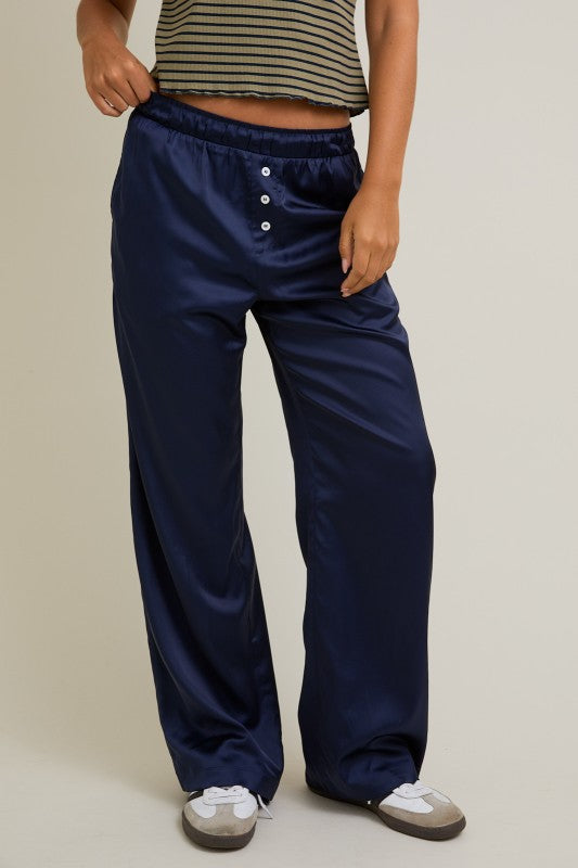Navy satin pajama pants worn by a person on a beige background