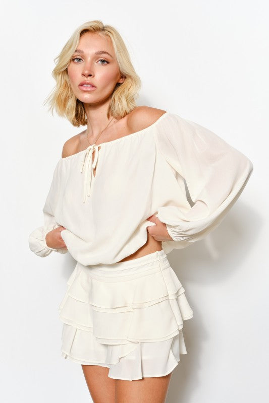 Woman wearing a white off-shoulder top and skirt against a plain background