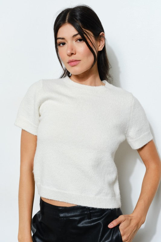Woman wearing a white knit top and black pants against a plain background