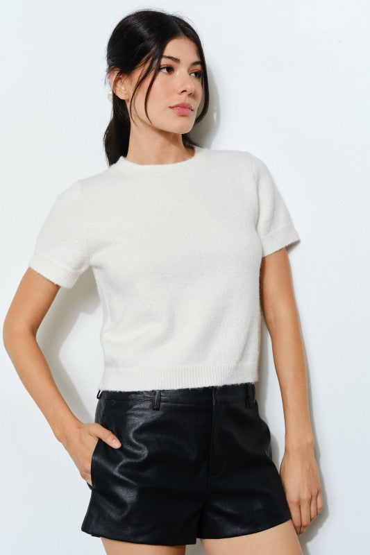 Woman wearing a white sweater and black leather shorts against a white background