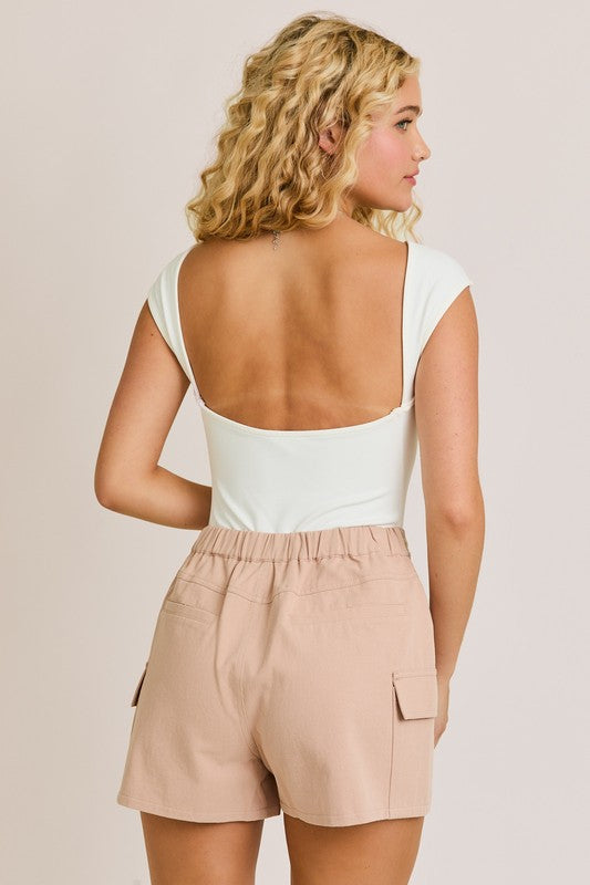 Woman wearing a white top and beige shorts against a plain background