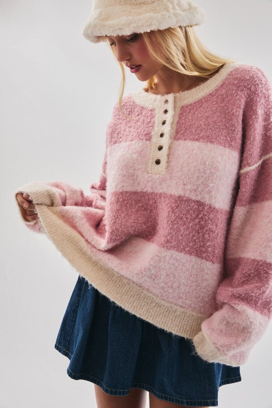 Woman wearing a pink and beige striped sweater with a denim skirt on a plain background